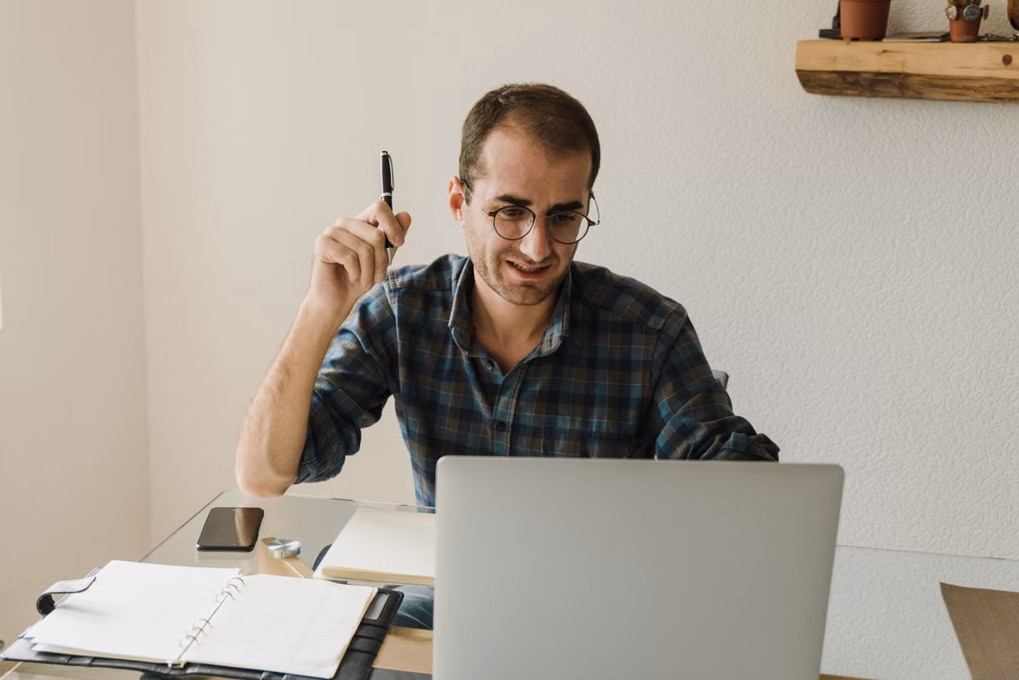 A man working at a laptop with a pen in his hand.
