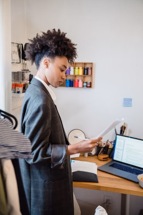A person reviewing papers beside an open laptop at a desk.